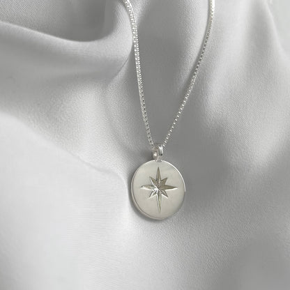 Silver necklace with a round pendant featuring a star design on a light gray fabric background