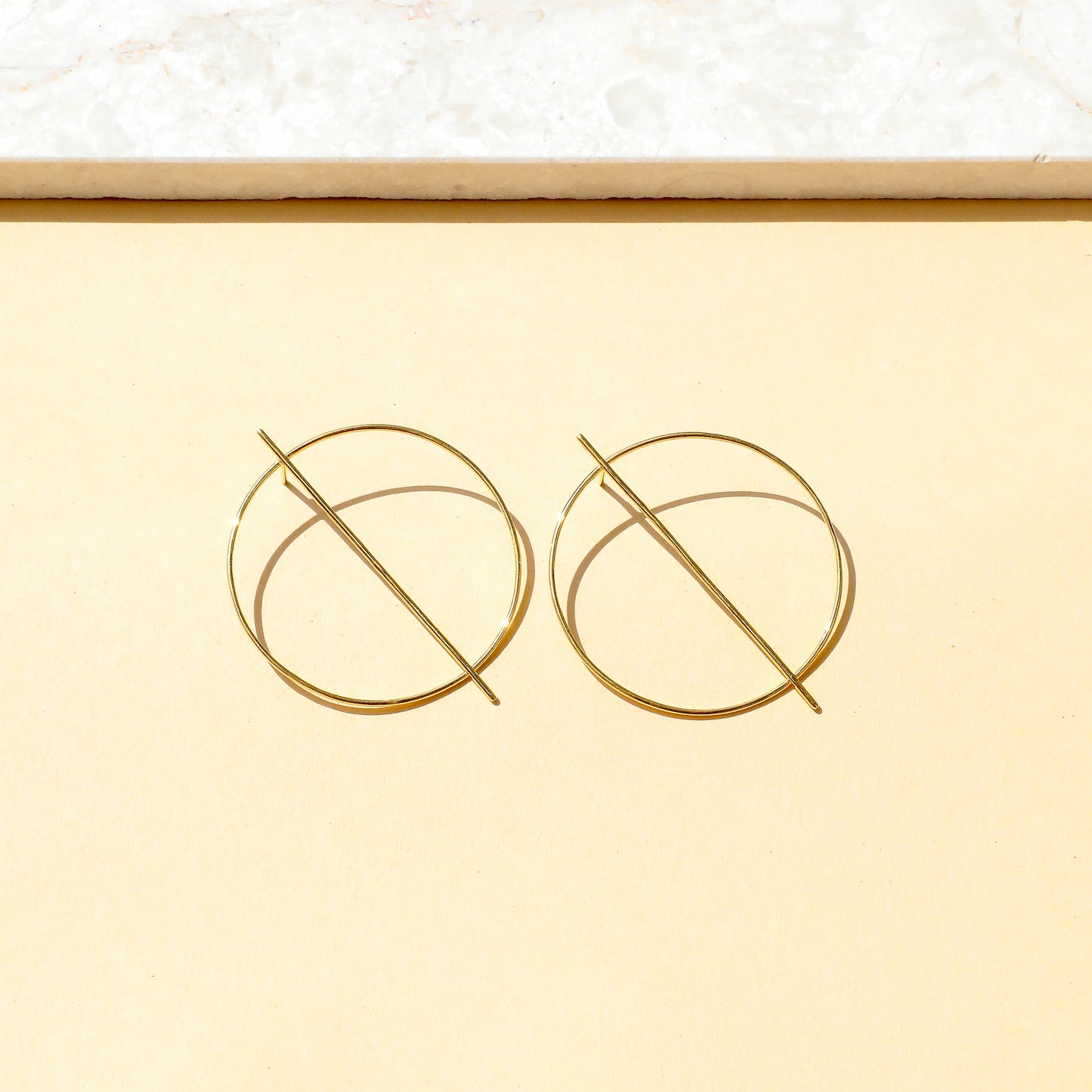 Gold circular earrings on a light yellow background