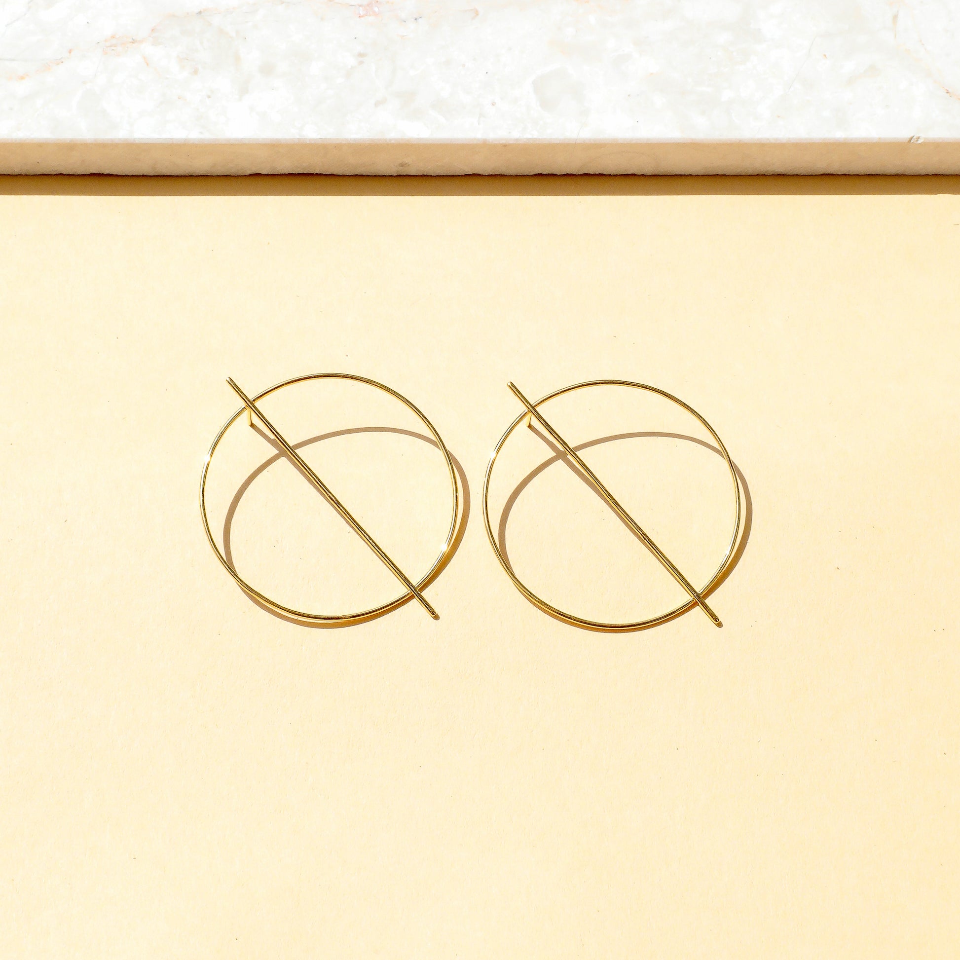 Gold circular earrings on a light yellow background