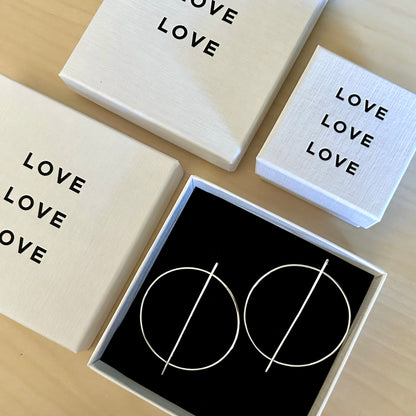 Circular silver earrings and set of boxes with 'LOVE' text and a black box with geometric design on a wooden surface