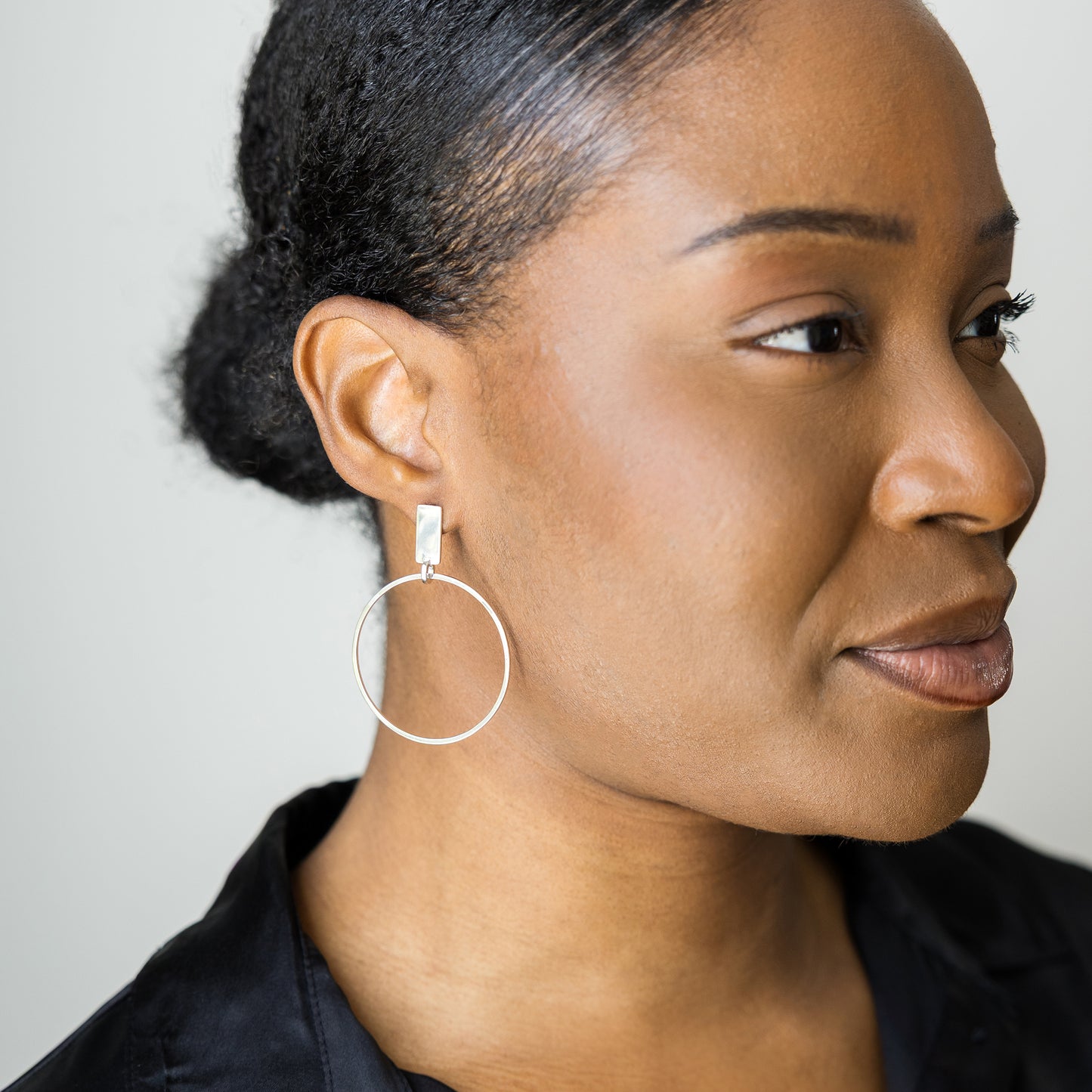 Close-up of a woman wearing hoop earrings with a neutral background