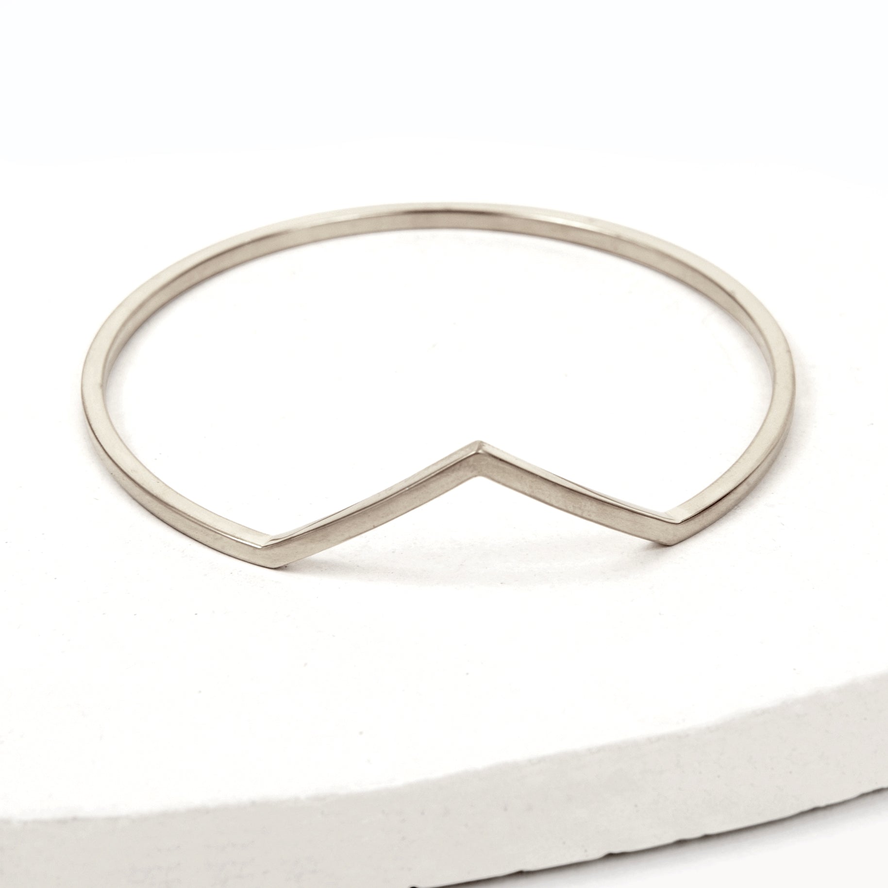Silver bangle bracelet with triangle shaped V peak against a white background