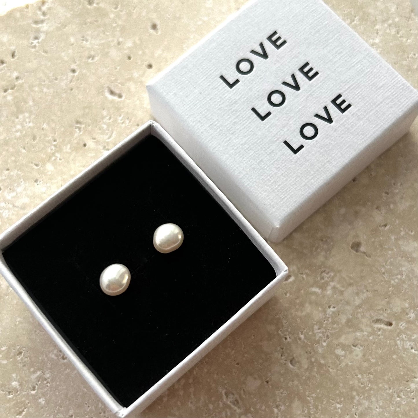 Pair of pearl earrings in a box with 'LOVE' text on a beige surface