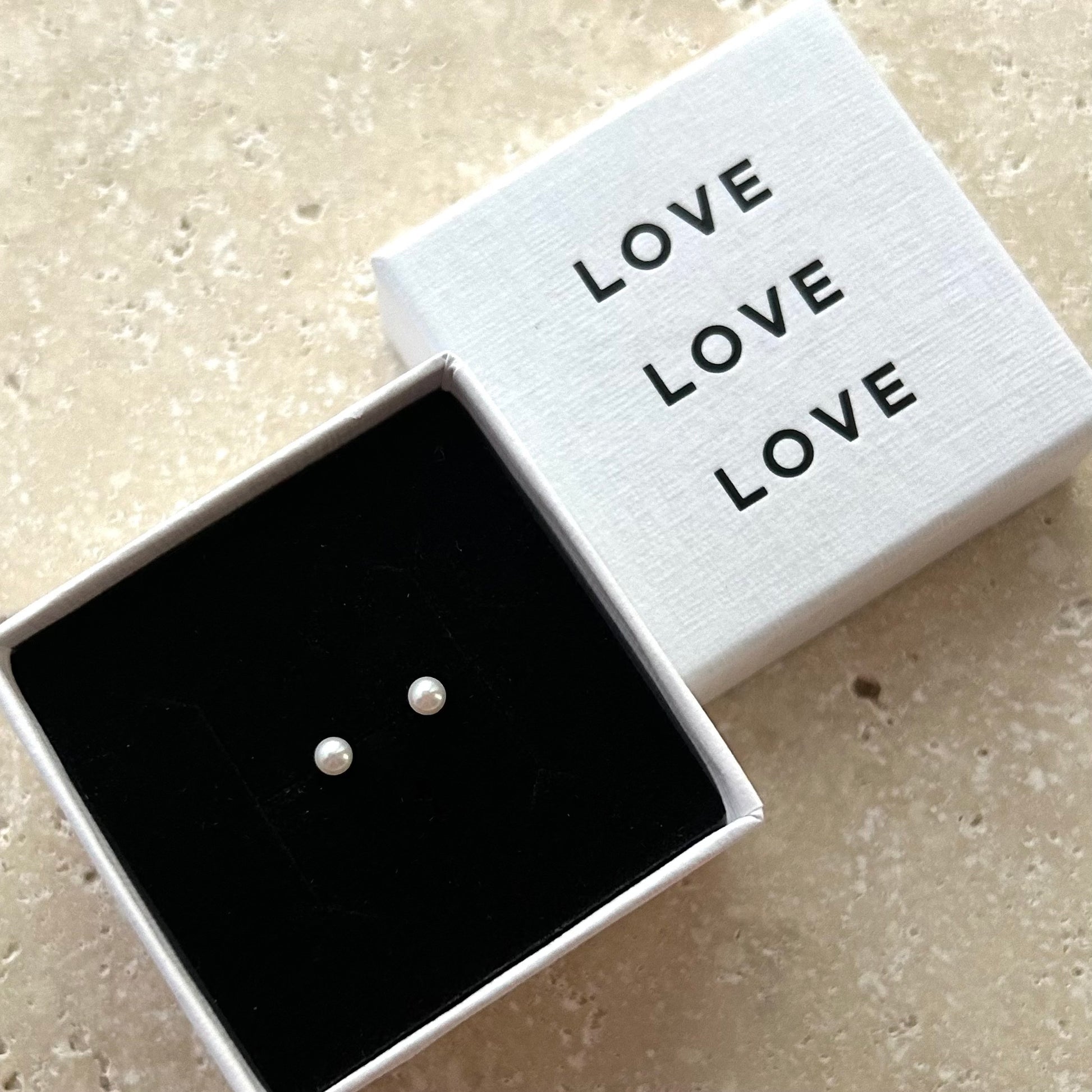 Pearl stud earrings in a box with 'LOVE' text on a beige background