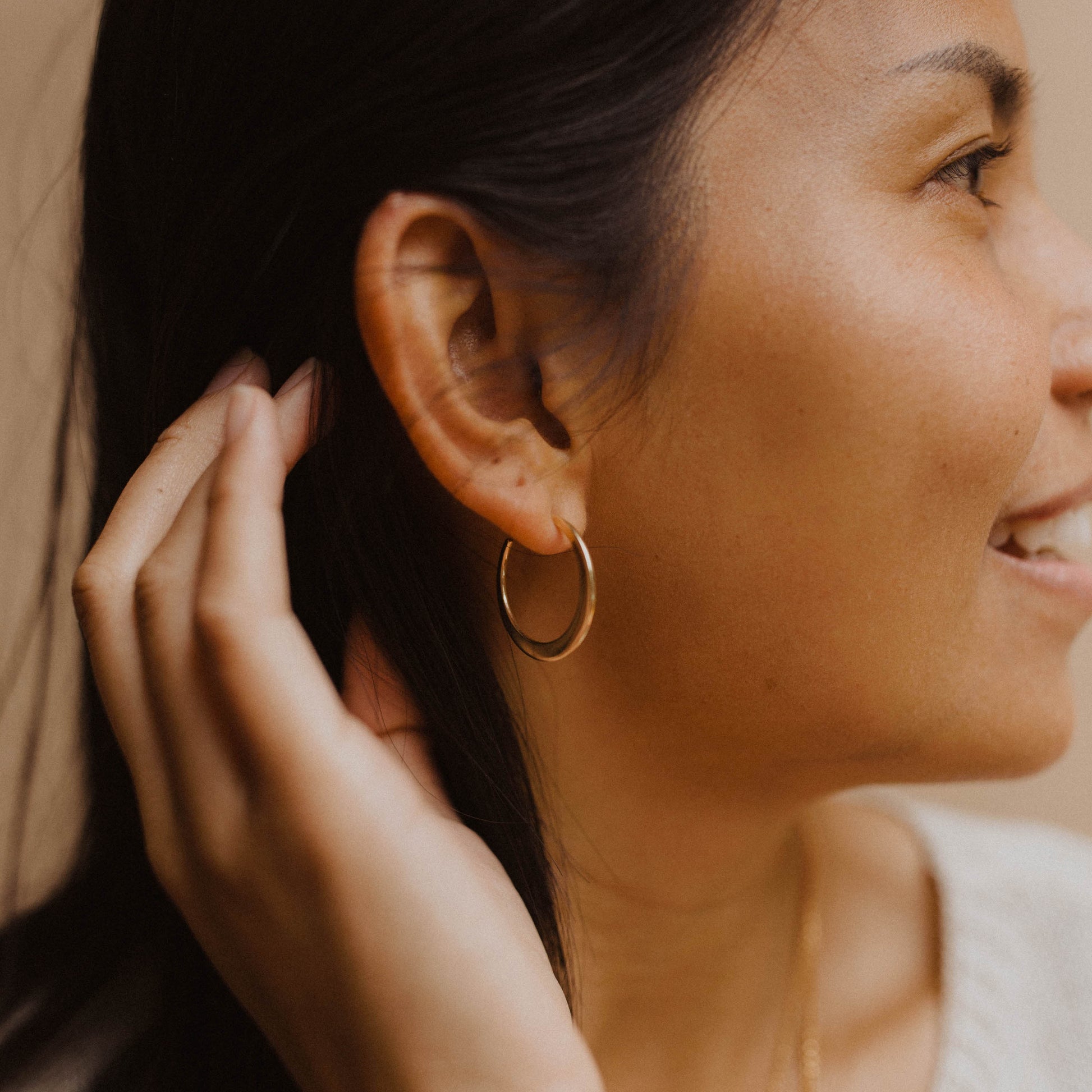 Person wearing a gold hoop earring in front of a neutral background