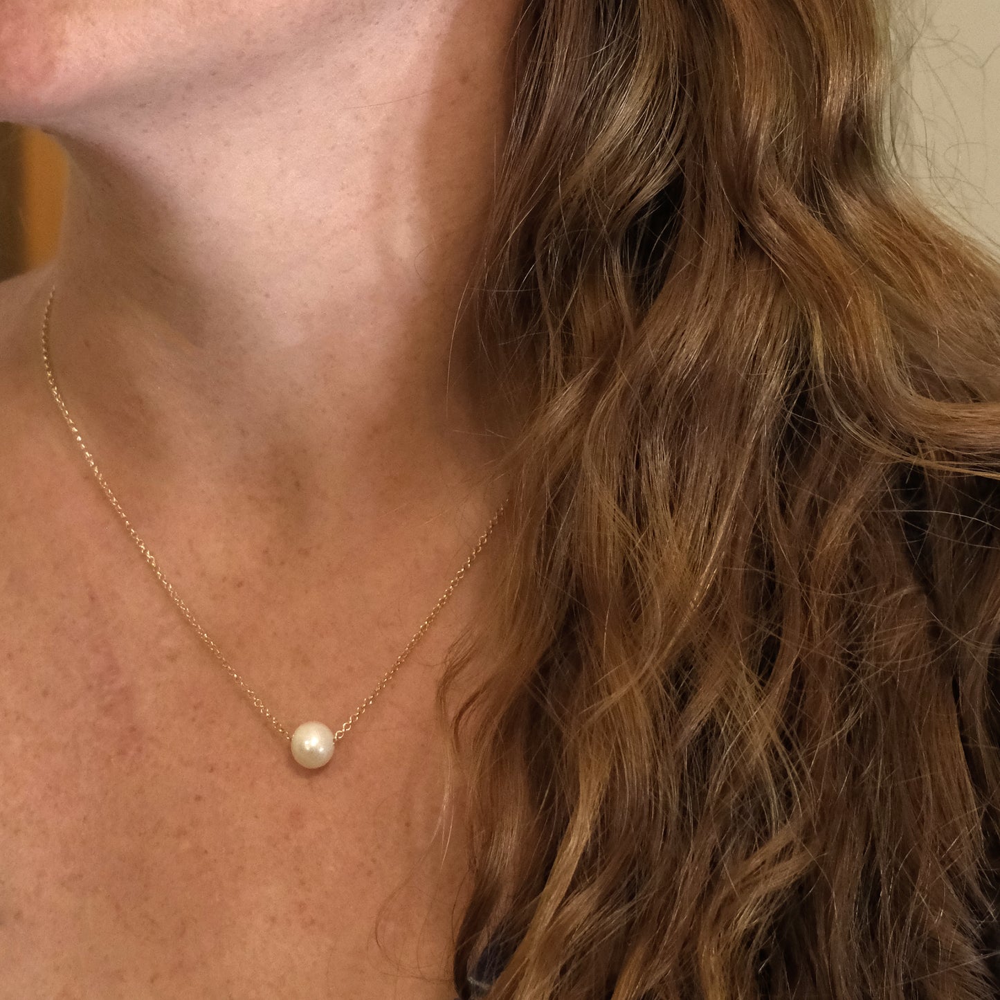 Close-up of a person wearing a gold necklace with a pearl pendant.