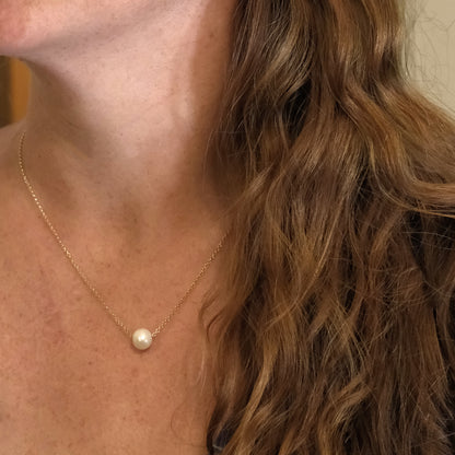 Close-up of a person wearing a gold necklace with a pearl pendant.