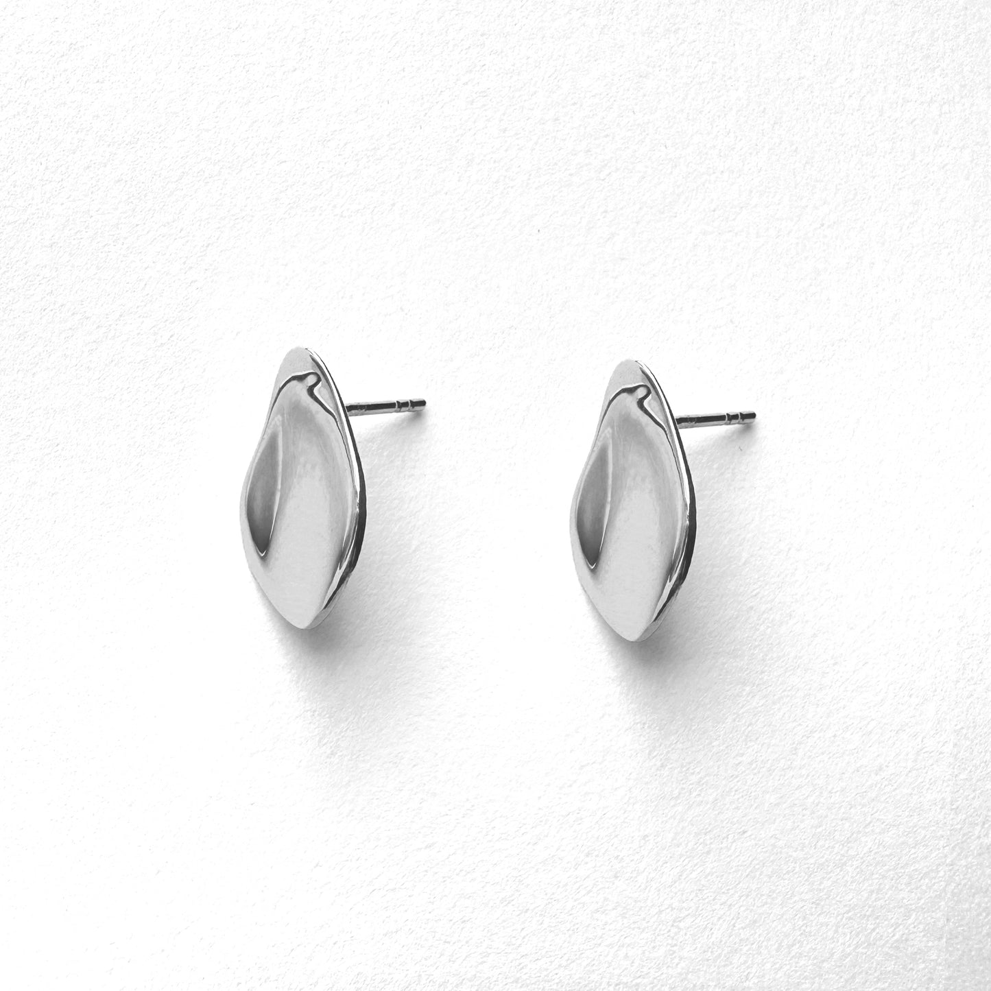 A pair of petal-shaped silver stud earrings against a white background