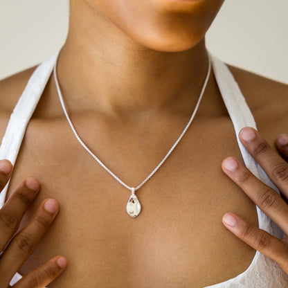 Person wearing a silver necklace with a teardrop pendant
