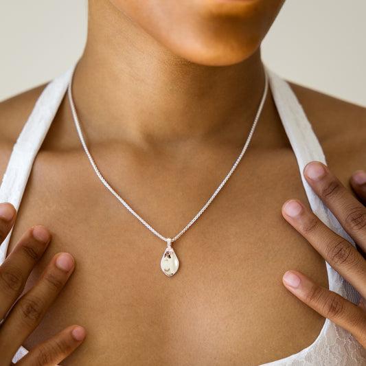 Person wearing a silver necklace with a teardrop pendant