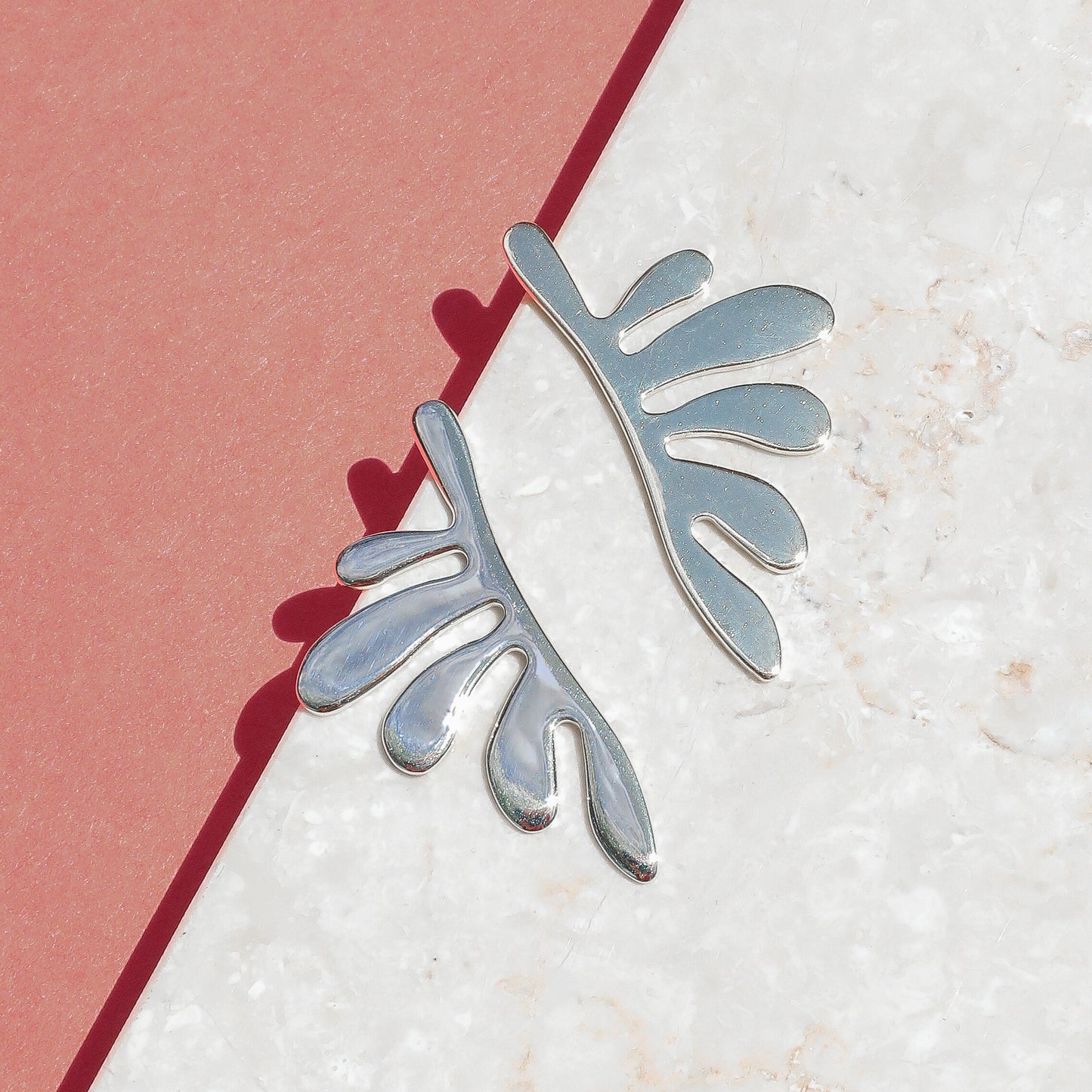 A pair of silver leaf-shaped earrings against a white background