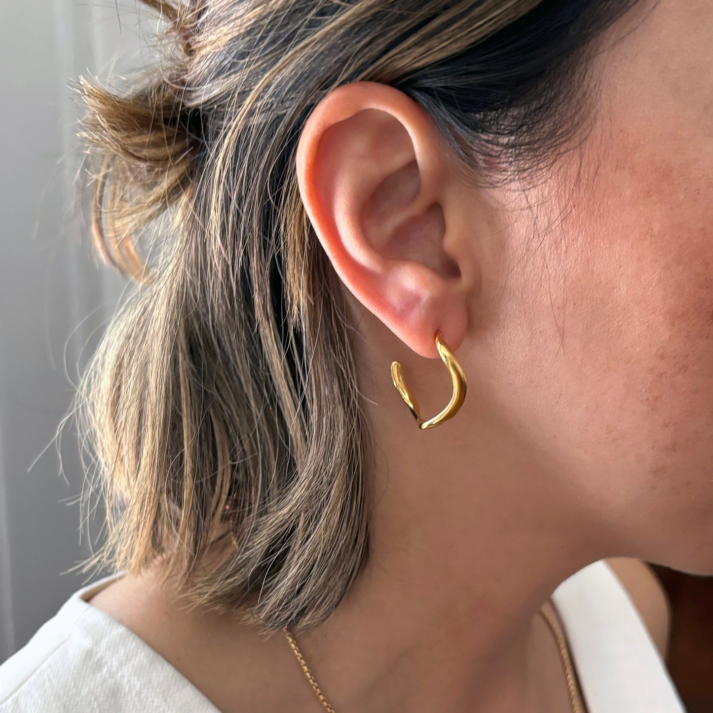 Close-up of a person wearing gold hoop earrings with a neutral background