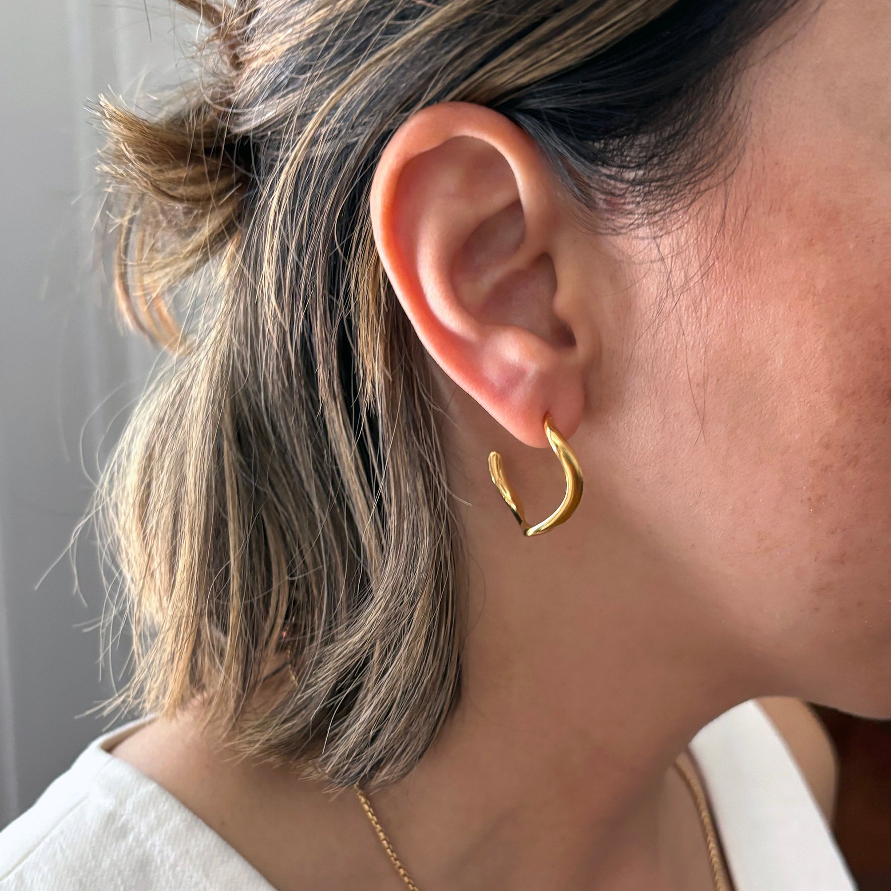 Close-up of a person wearing gold hoop earrings with a neutral background