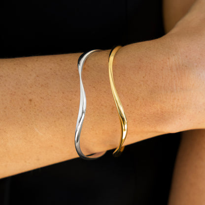 Gold and silver bangles on a wrist against a black background