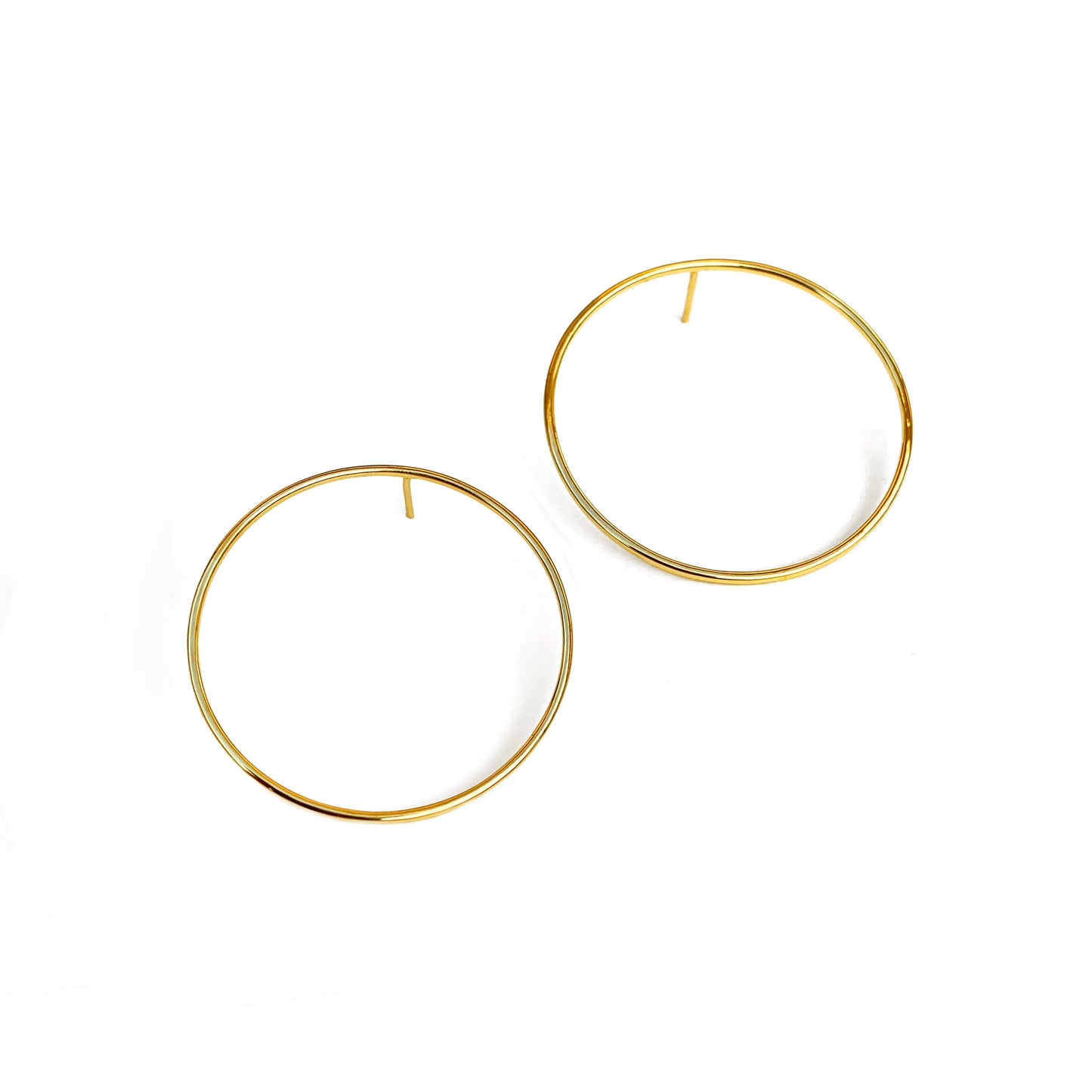 A pair of large, circular, gold earrings positioned against a white background.