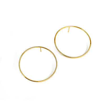 A pair of large, circular, gold earrings positioned against a white background.