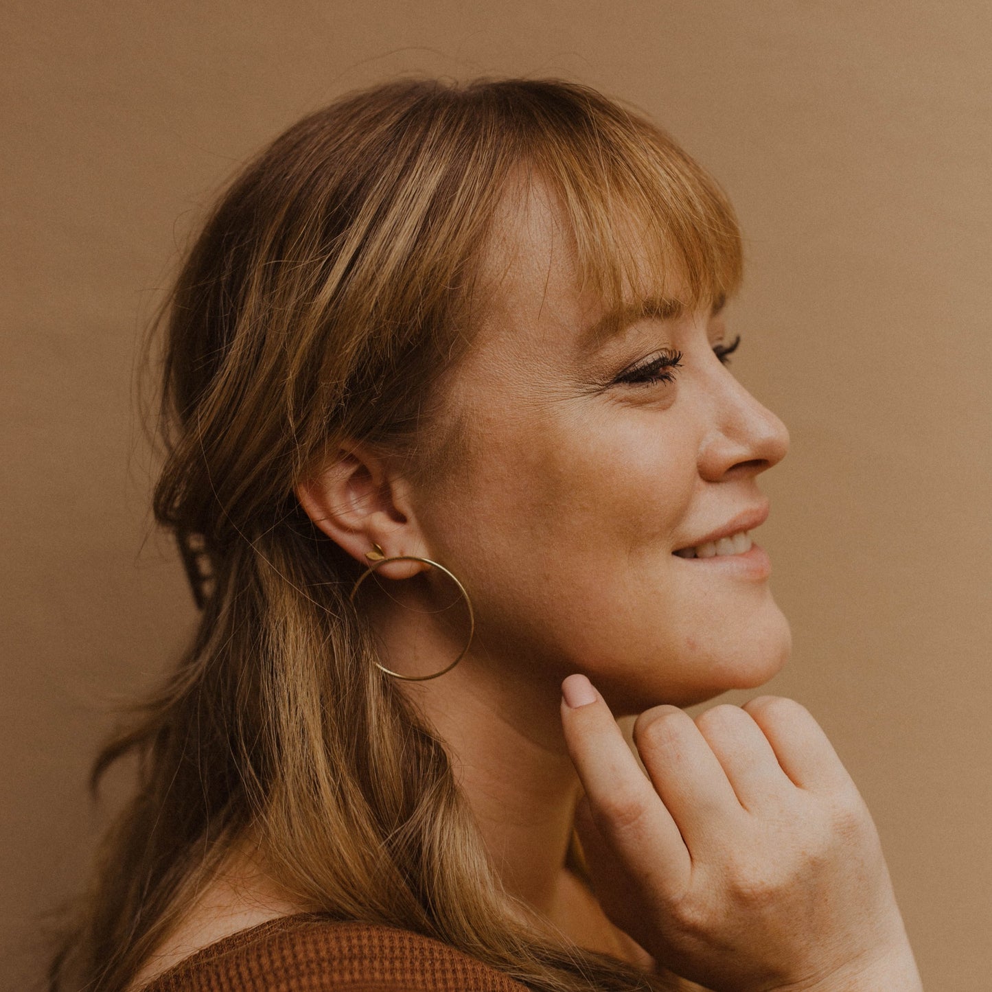 Person wearing a gold hoop earring with a neutral background