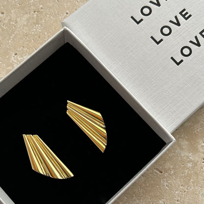 Gold geometric shell earrings in a 'LOVE' branded box on a beige surface