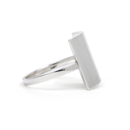 A silver-colored modern square ring with a shield shape design on a white background.