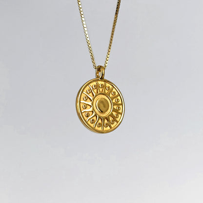Gold necklace with a circular pendant on a light gray background