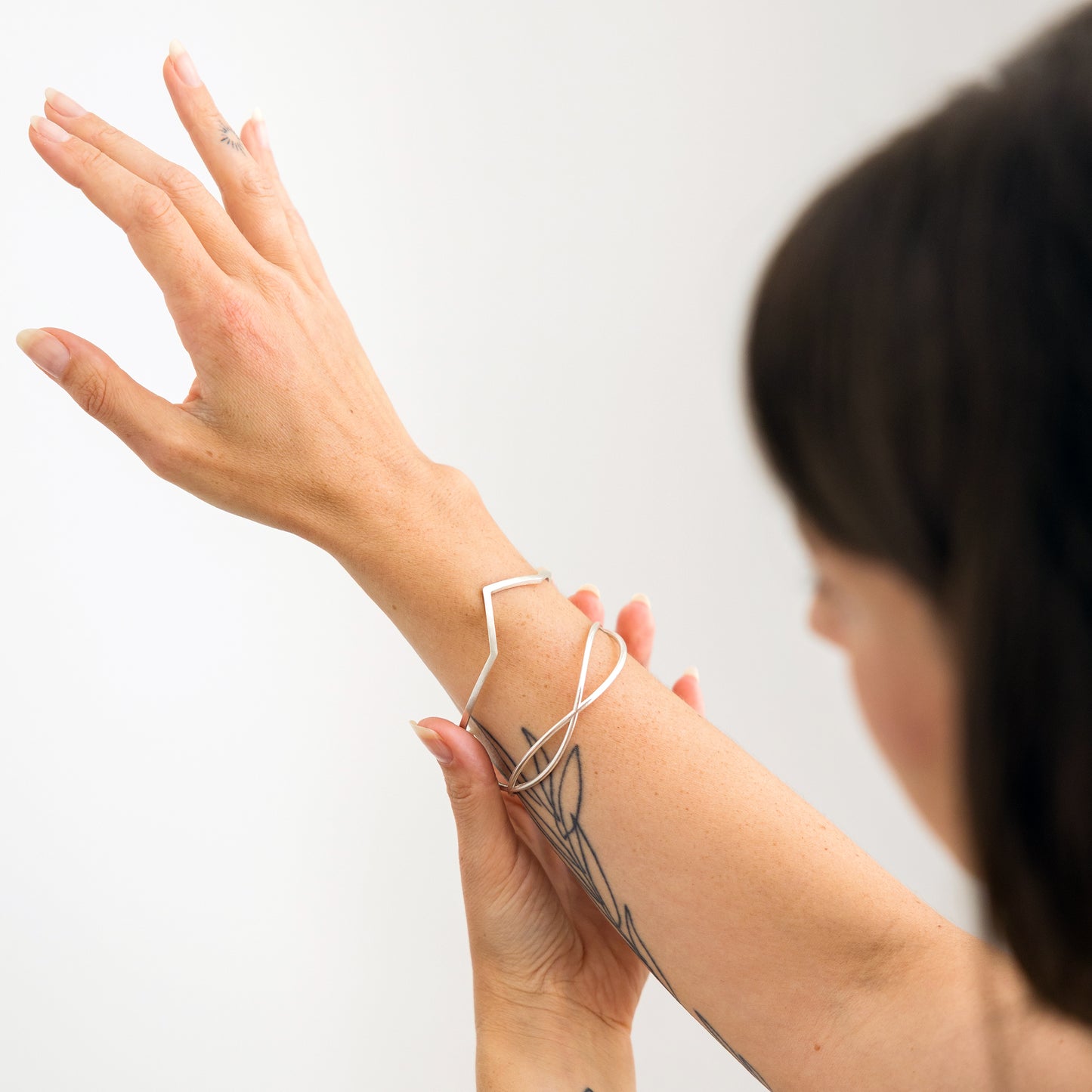 Person wearing a two silver bracelets on a plain background