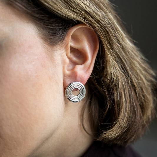 Close-up of an ear wearing a silver earring with concentric circles.