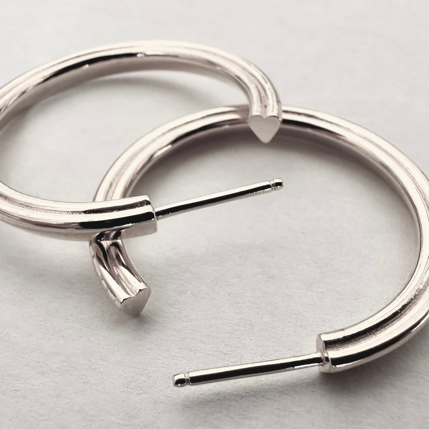 Close up of silver hoop earrings with a hidden heart design against a white background