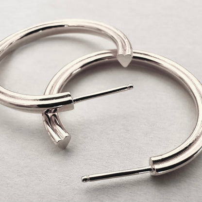 Close up of silver hoop earrings with a hidden heart design against a white background