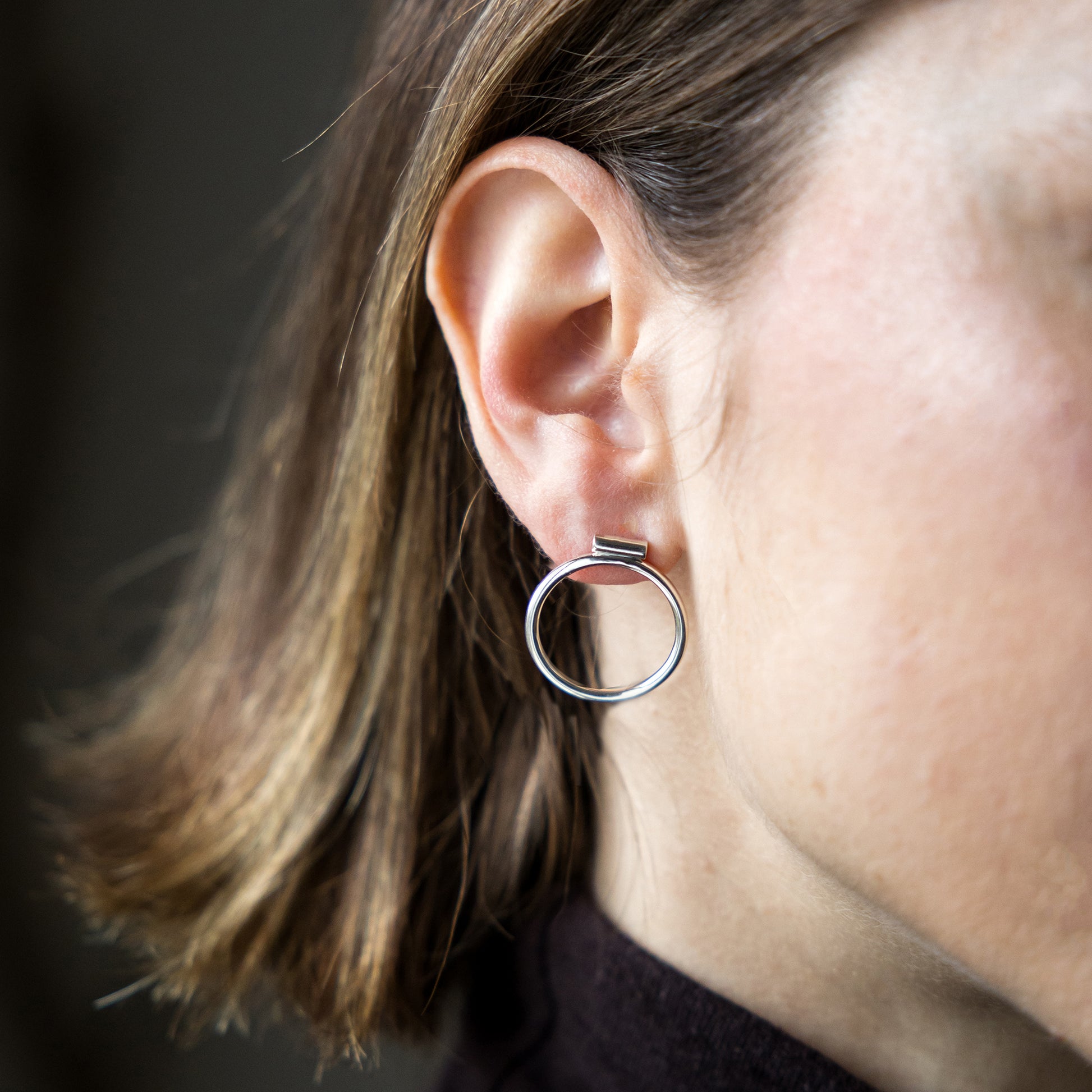 Close-up of a person wearing a silver hoop earring with a dark background