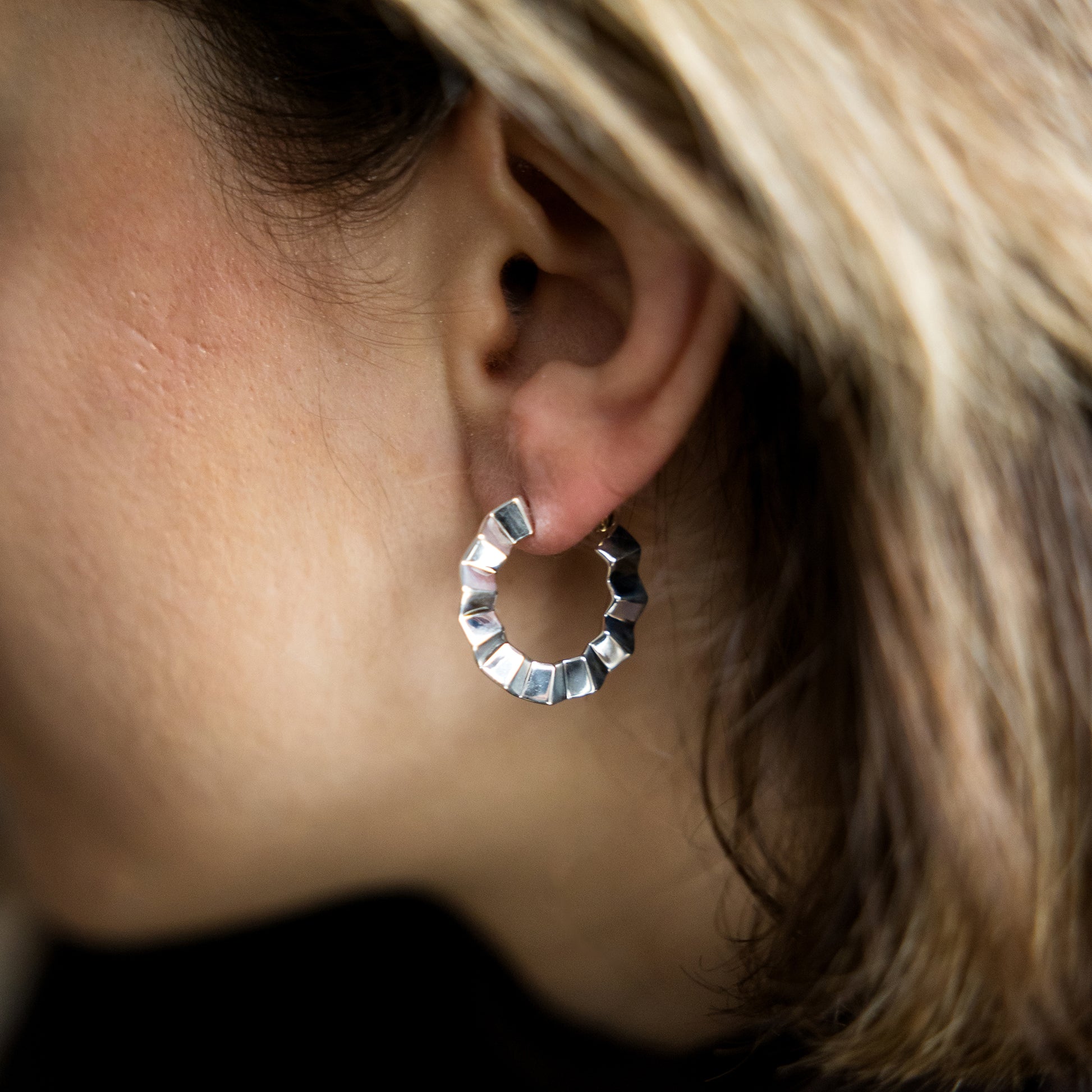 Close-up of a silver hoop earring worn by a person with blonde hair.