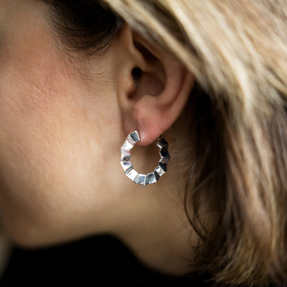 Close-up of a silver hoop earring worn by a person with blonde hair.