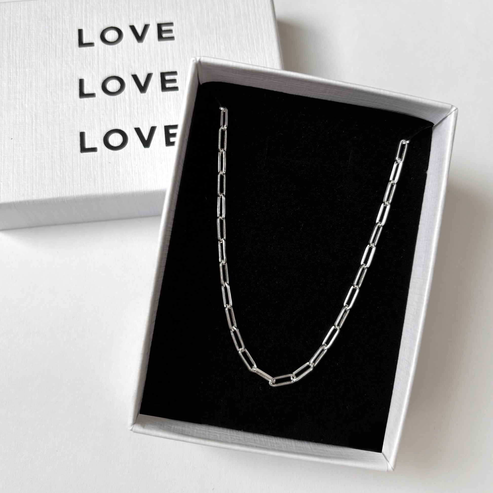 Silver necklace in a box with 'LOVE' text on a white background