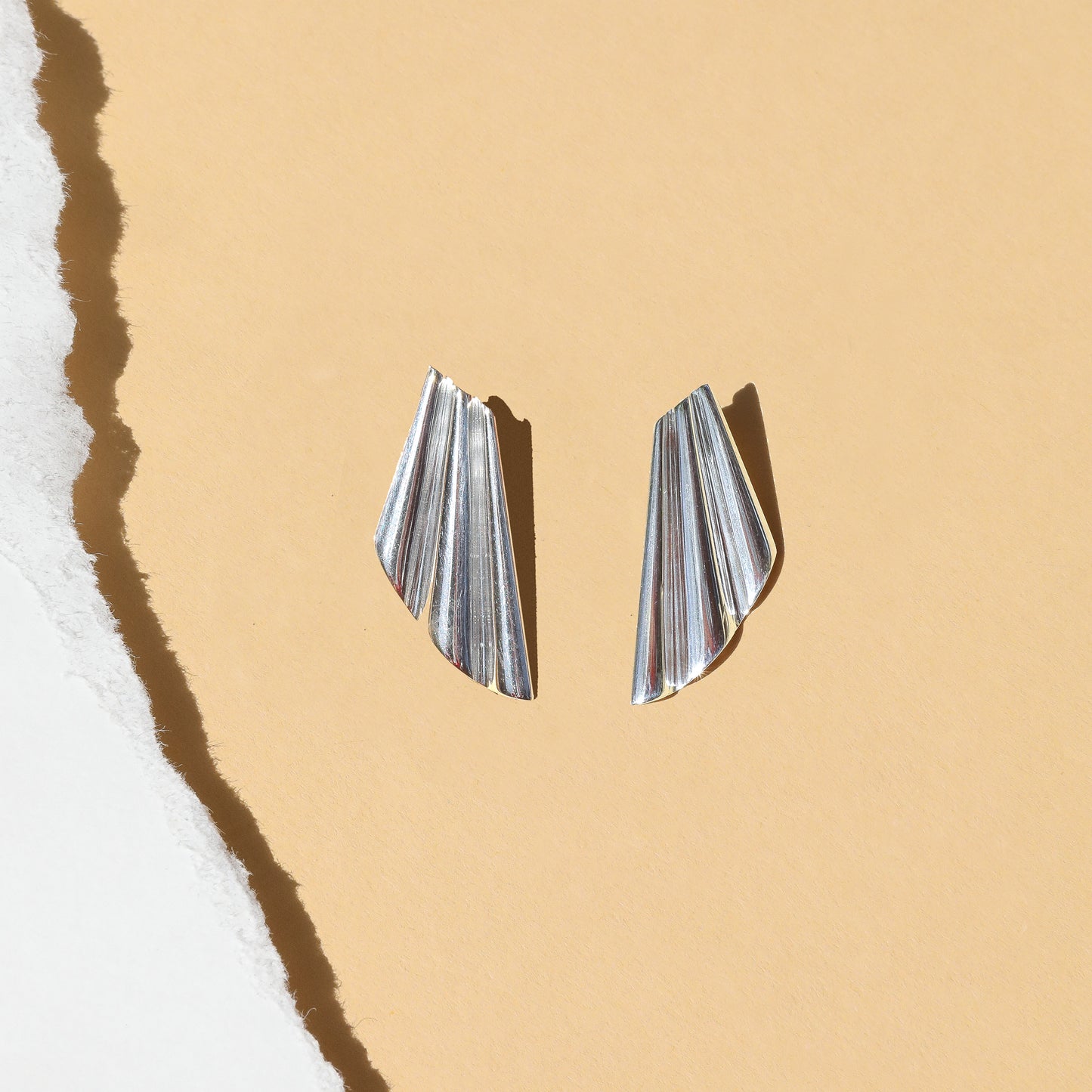 A pair of silver-colored modern wavy earrings designed to resemble seashell fragments.