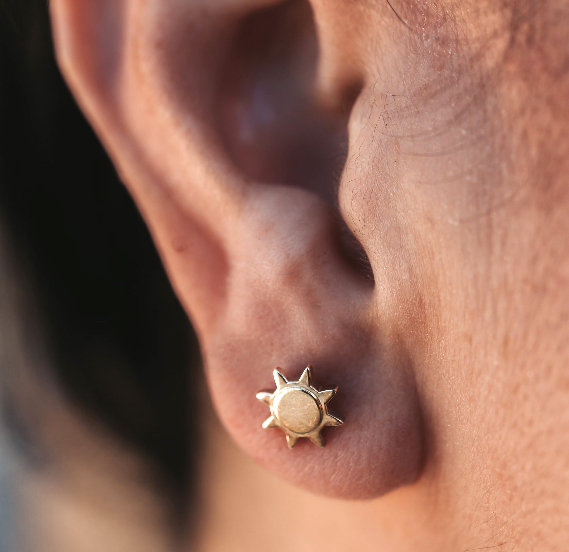 Close up of a person wearing a sun-shaped stud earring