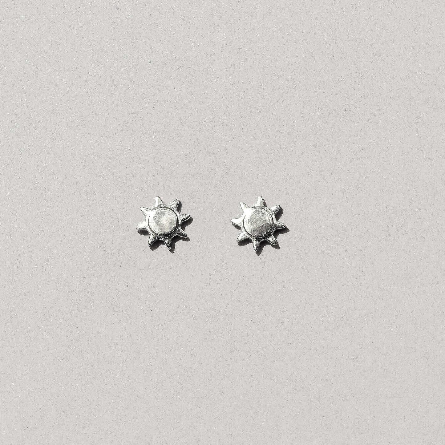 A pair of silver-colored sun stud earrings against a white background.