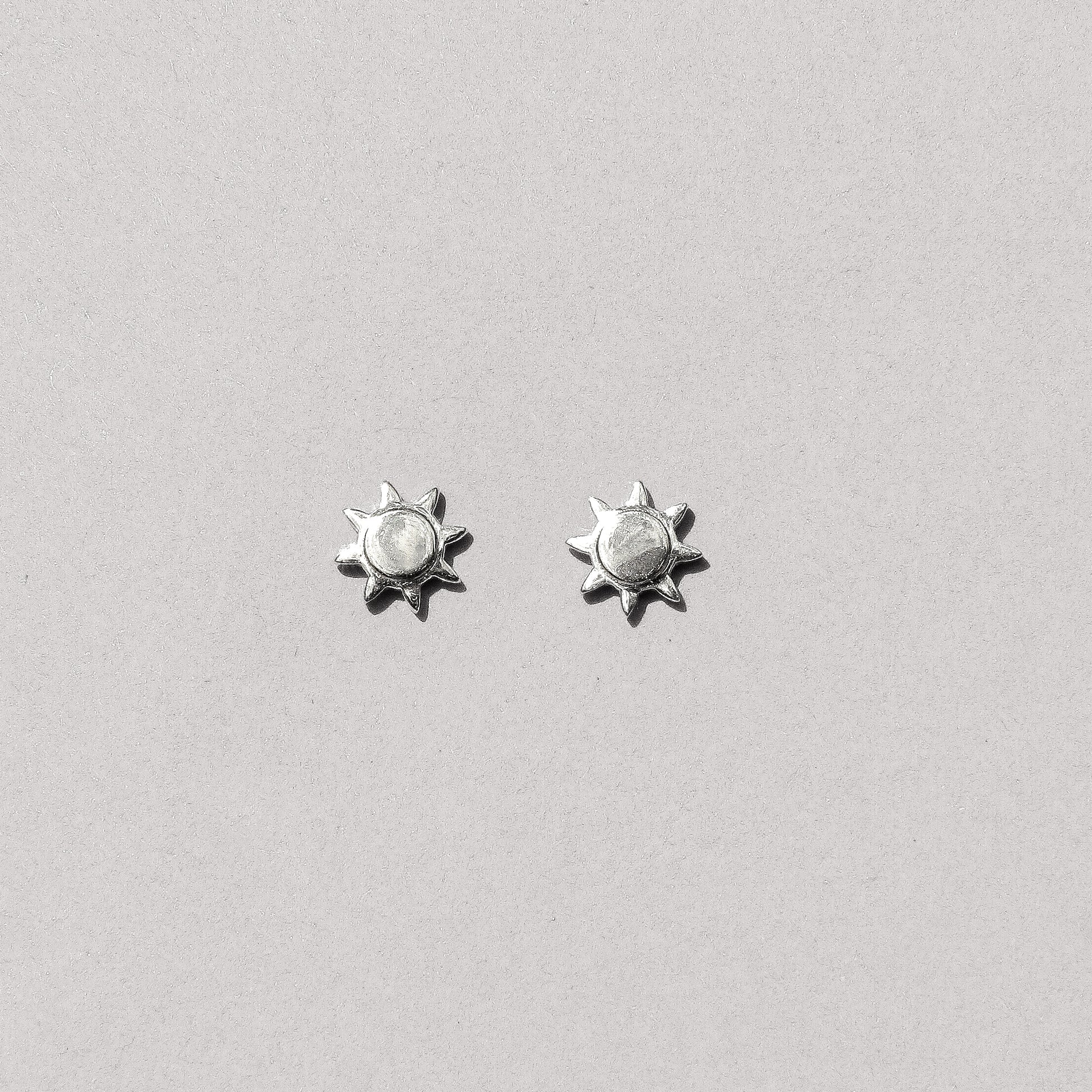 A pair of silver-colored sun stud earrings against a white background.