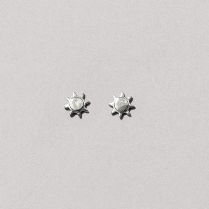A pair of silver-colored sun stud earrings against a white background.