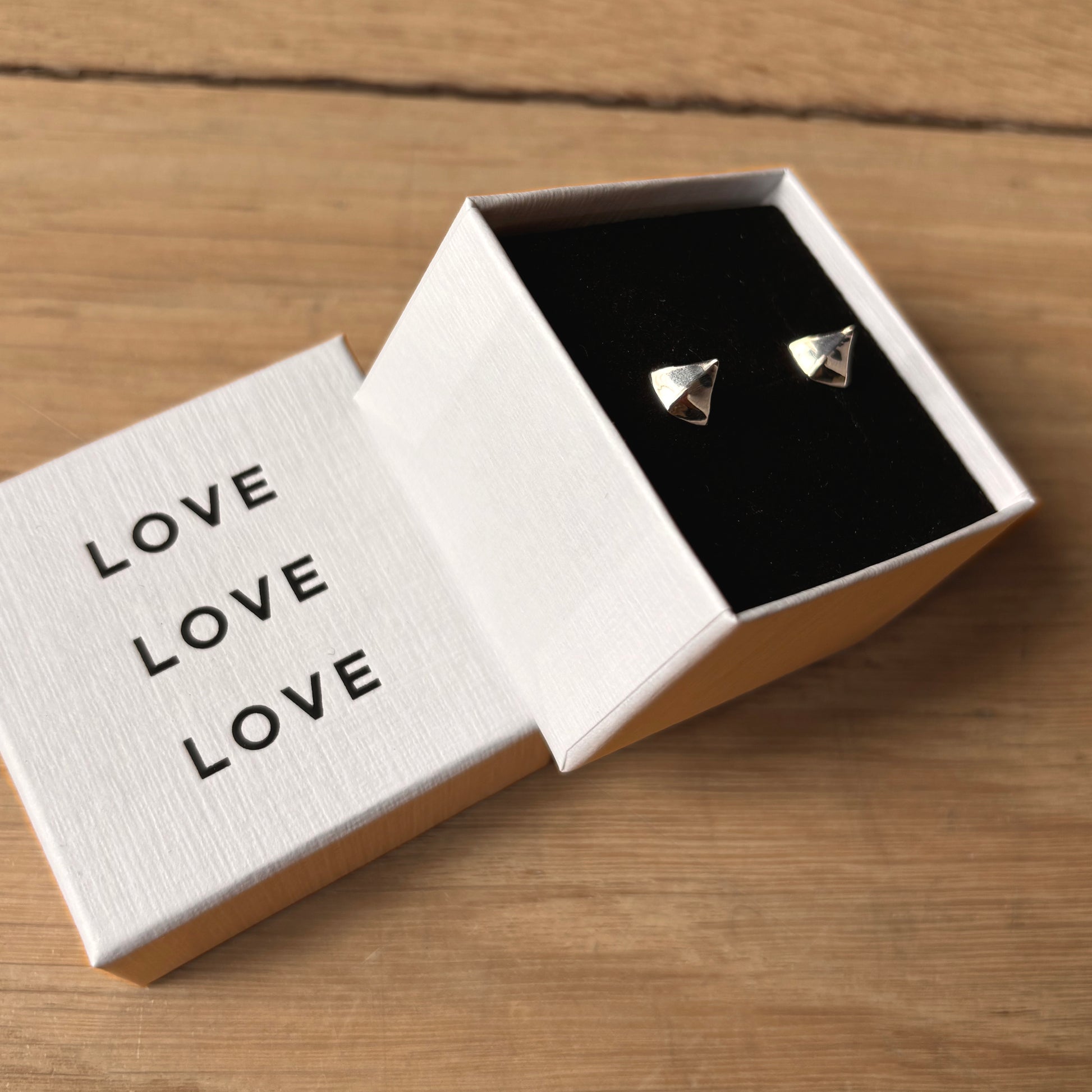 Triangular earrings in an open box with 'LOVE' text on a wooden surface