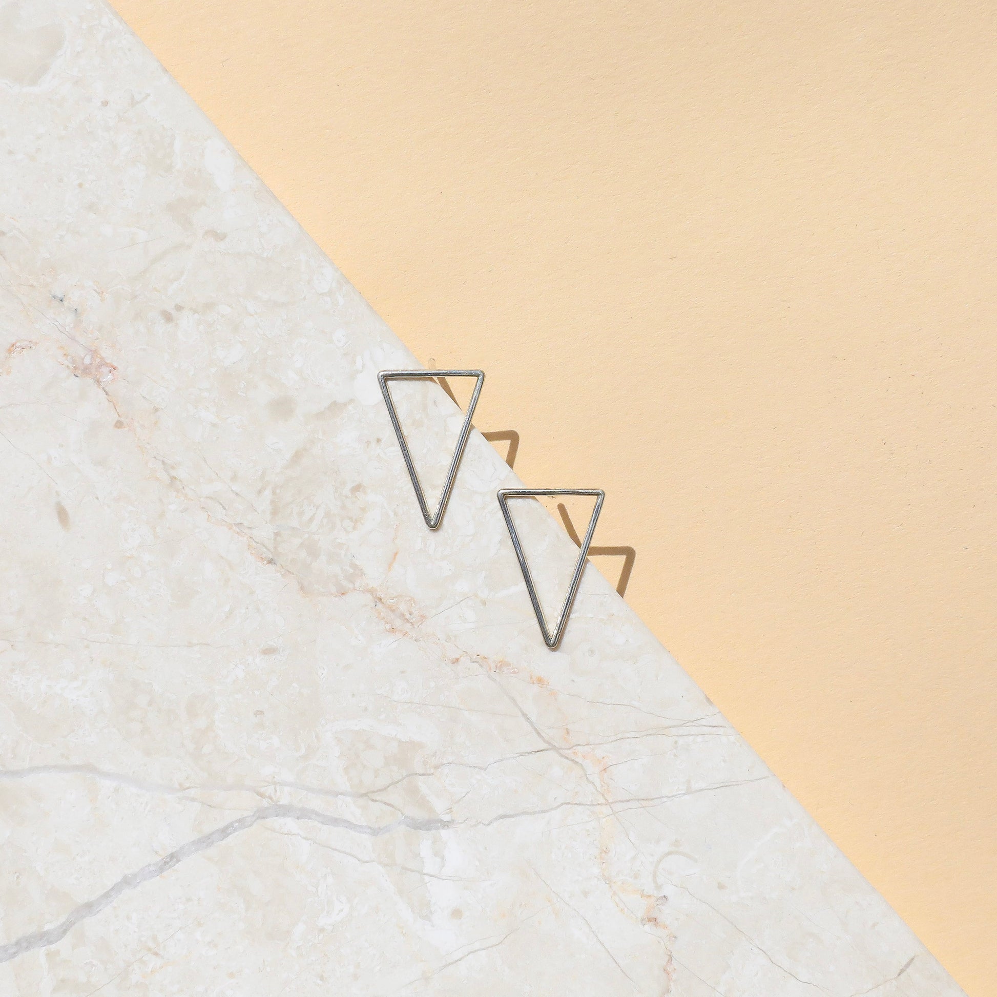 A pair of silver-colored open triangle earrings on a white background
