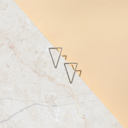 A pair of silver-colored open triangle earrings on a white background