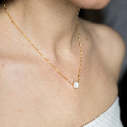 Gold necklace with a pearl pendant on a person wearing a white top.