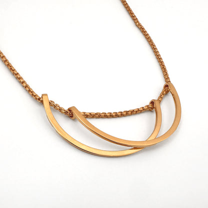 Close up of a gold necklace with two curved pendants against a white background