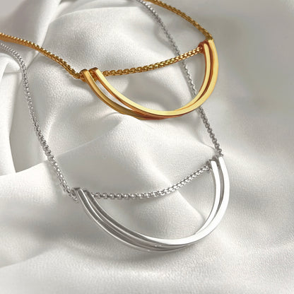 Two necklaces, one gold and one silver, on a white fabric background