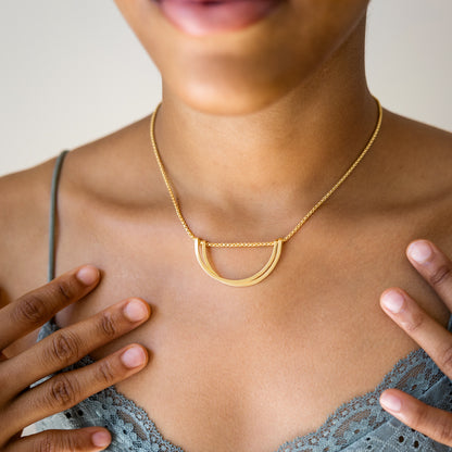 Gold necklace worn by a person against a neutral background