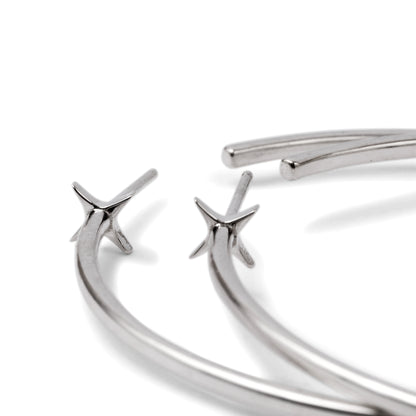 A pair of silver-colored hoop earrings with starburst designs attached to the hoops, positioned against a white background.