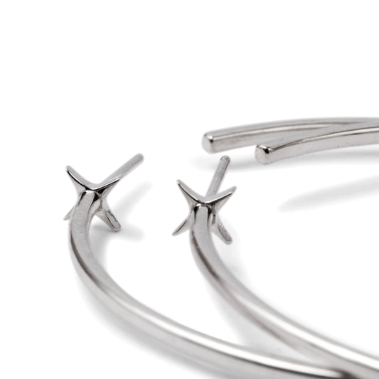A pair of silver-colored hoop earrings with starburst designs attached to the hoops, positioned against a white background.
