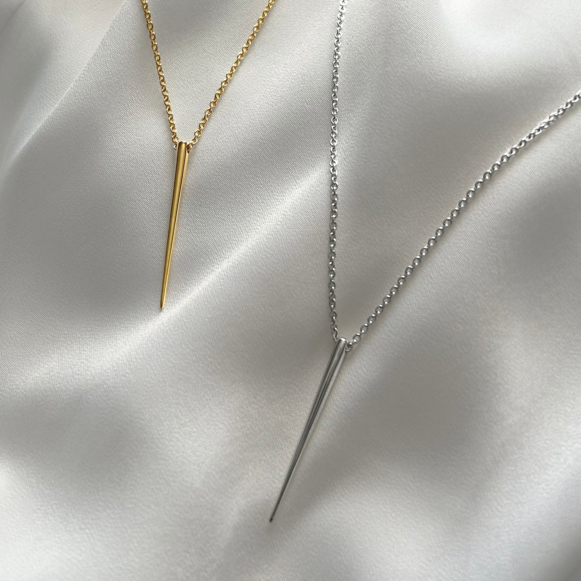 Two necklaces with spike pendants on a satin surface