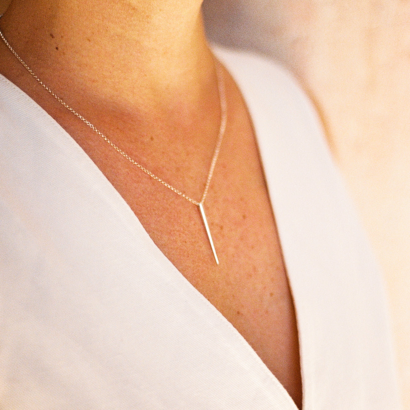 Person wearing a silver necklace with a long spike shaped pendant against a blurred background