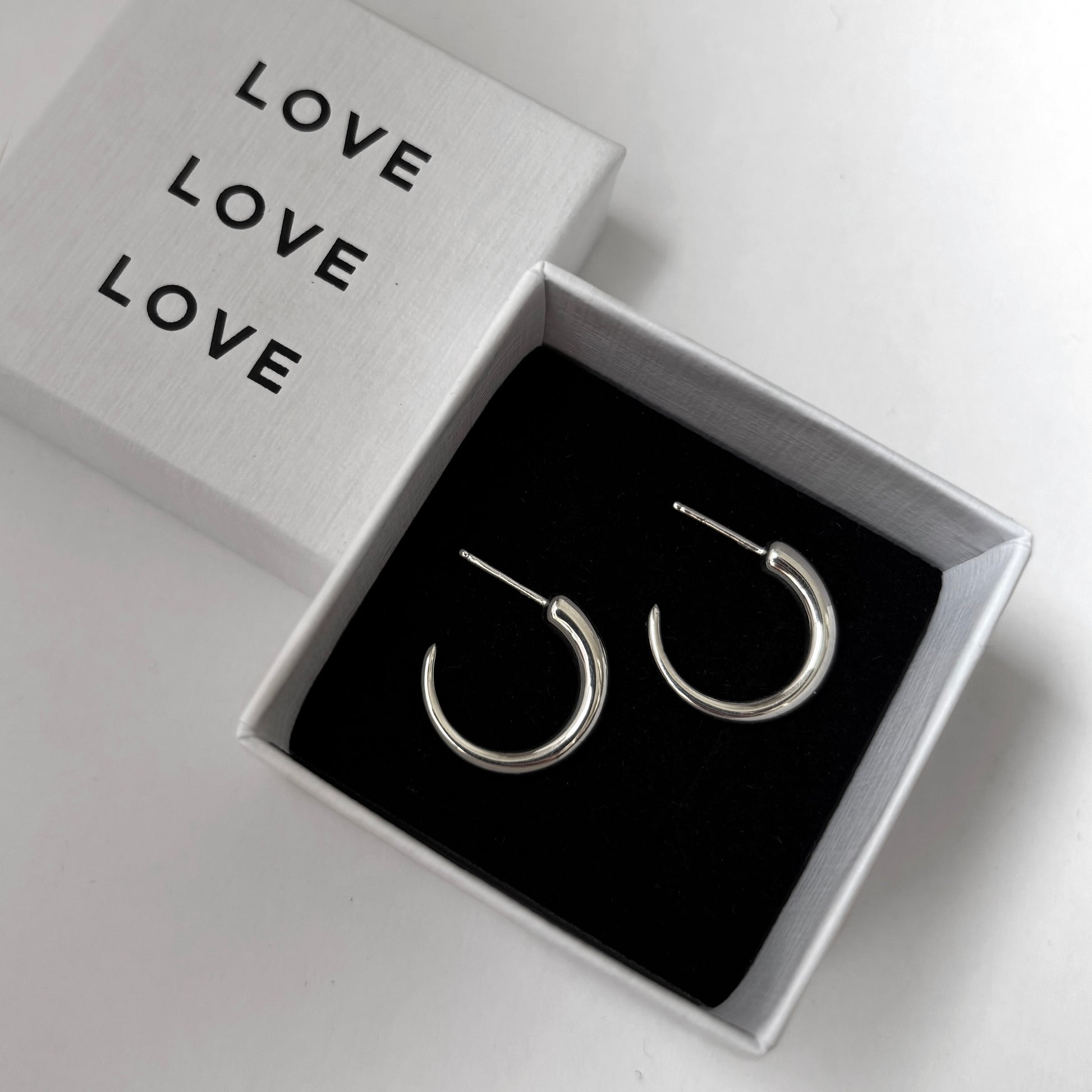 Silver hoop earrings in a box with 'LOVE' text on a light gray background