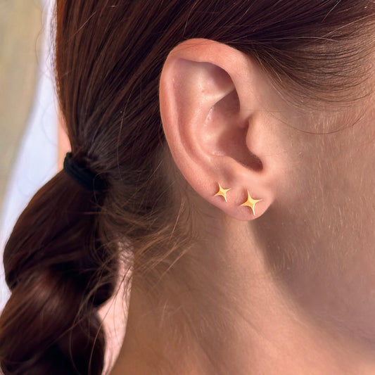 Close-up of an ear wearing gold star-shaped earrings with a blurred background